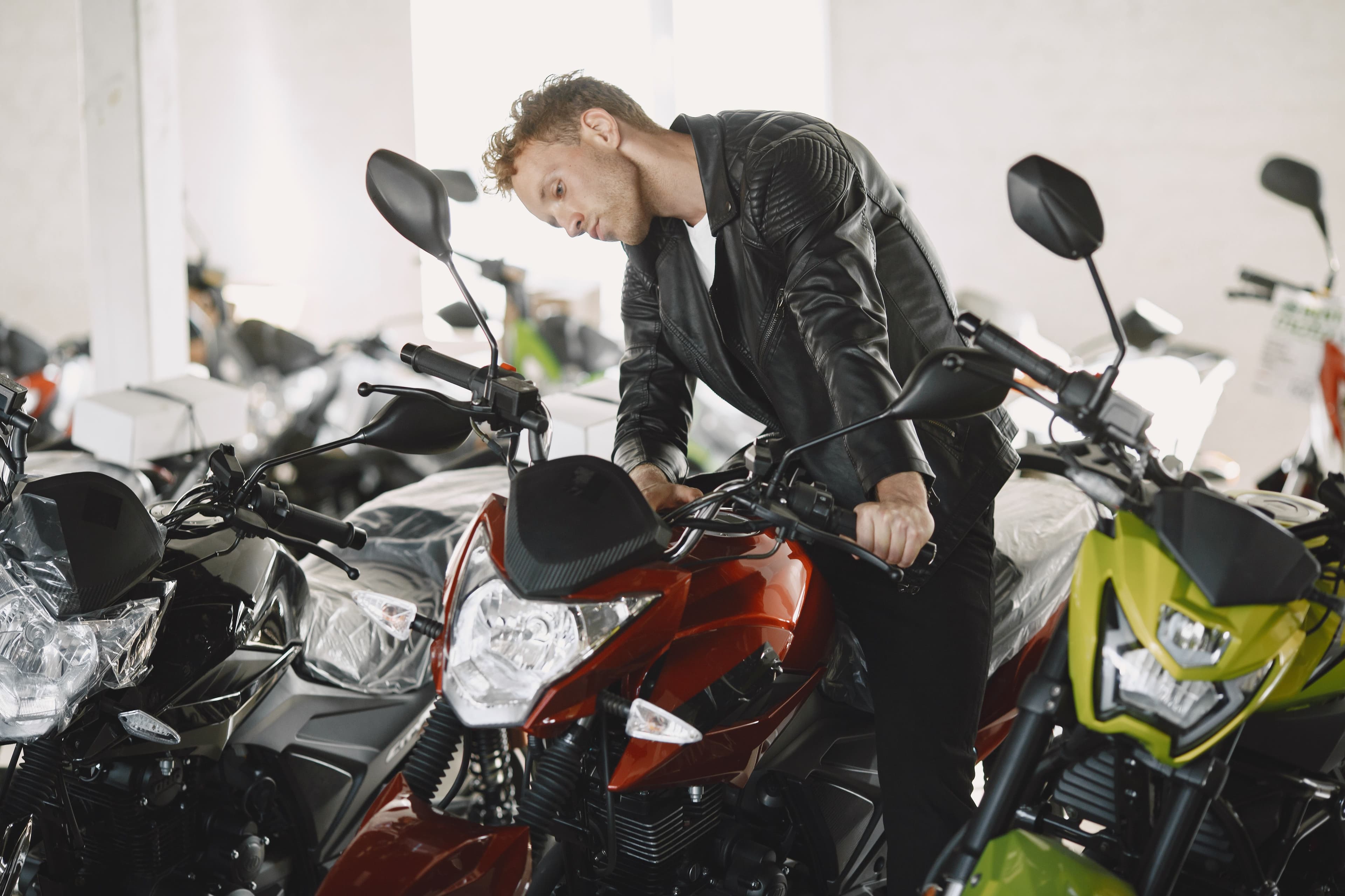 A first-time buyer talking with a salesperson beside a row of motorcycles inside a dealership showroom