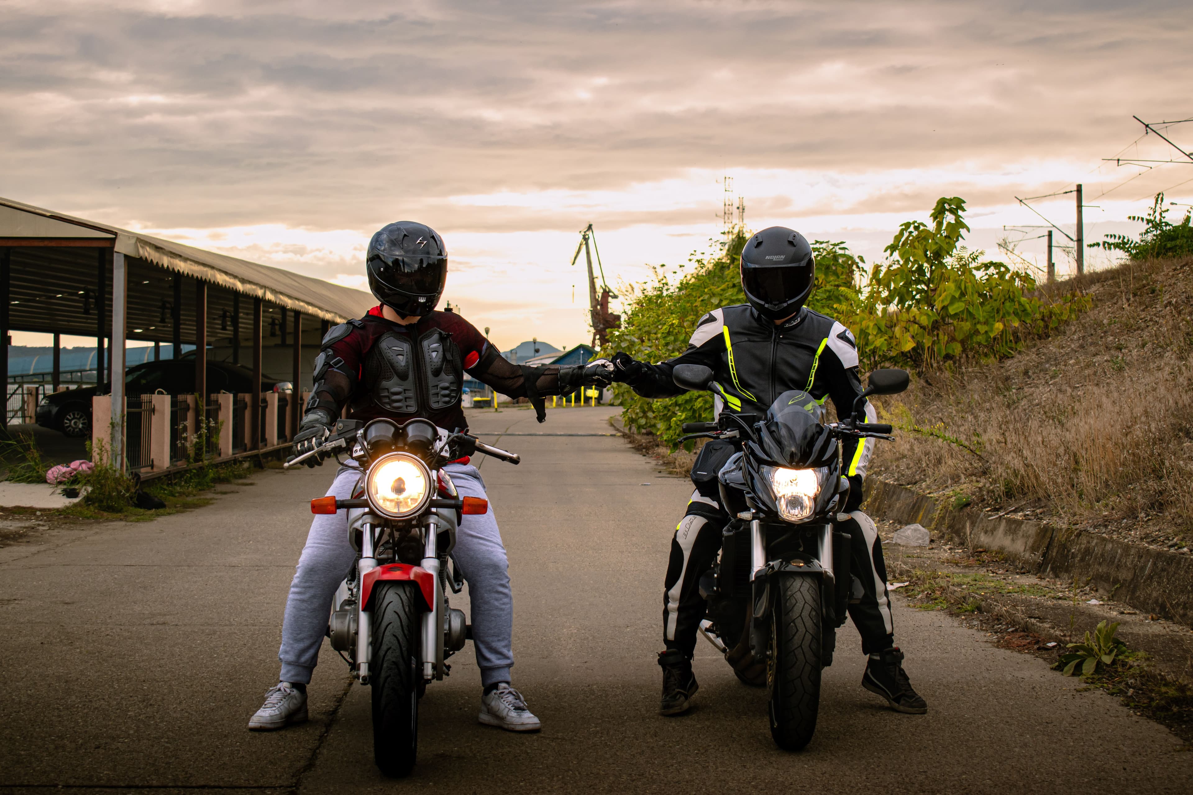 Two riders in full-face helmets sitting across a small cafe table over coffee, taking a break together