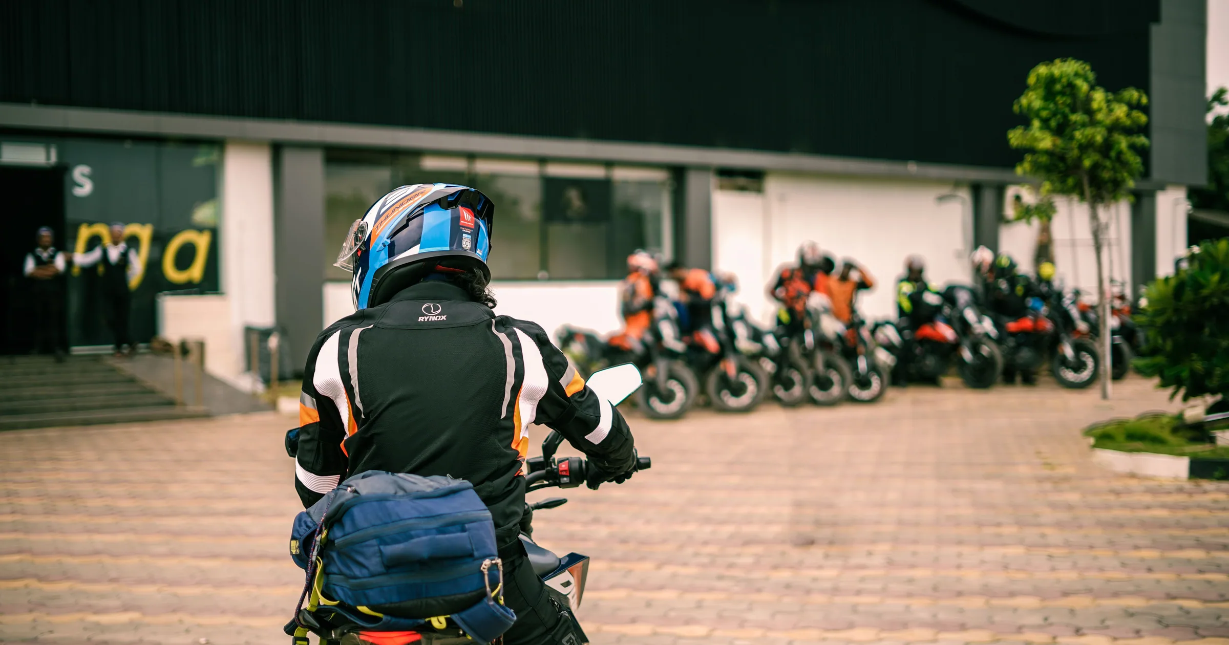 A rider arriving at a meeting point where a group of motorcycles is already staged before a ride