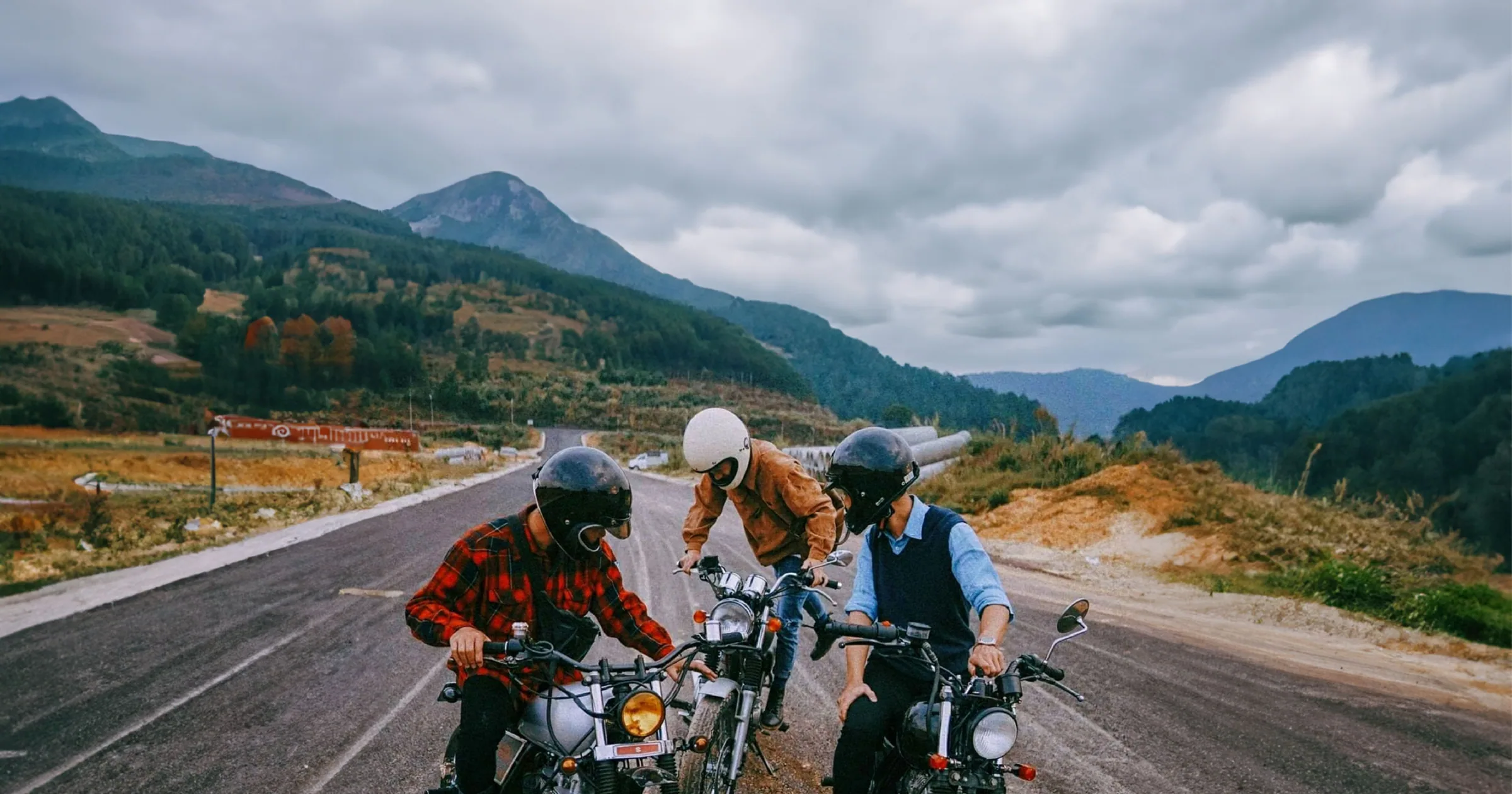 Three riders pausing with their motorcycles on a mountain road before continuing a group ride
