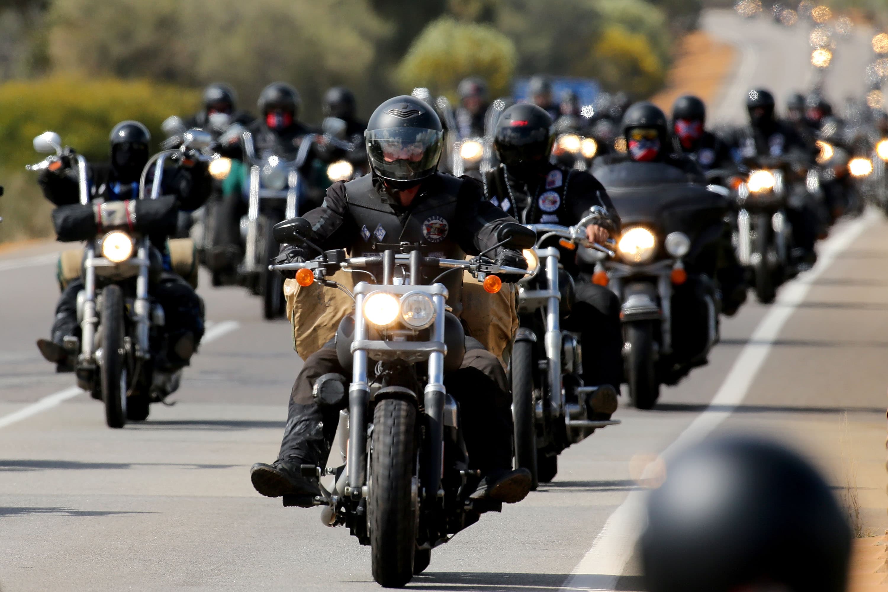 A large group of riders on cruisers travelling down an open highway together with their headlights on